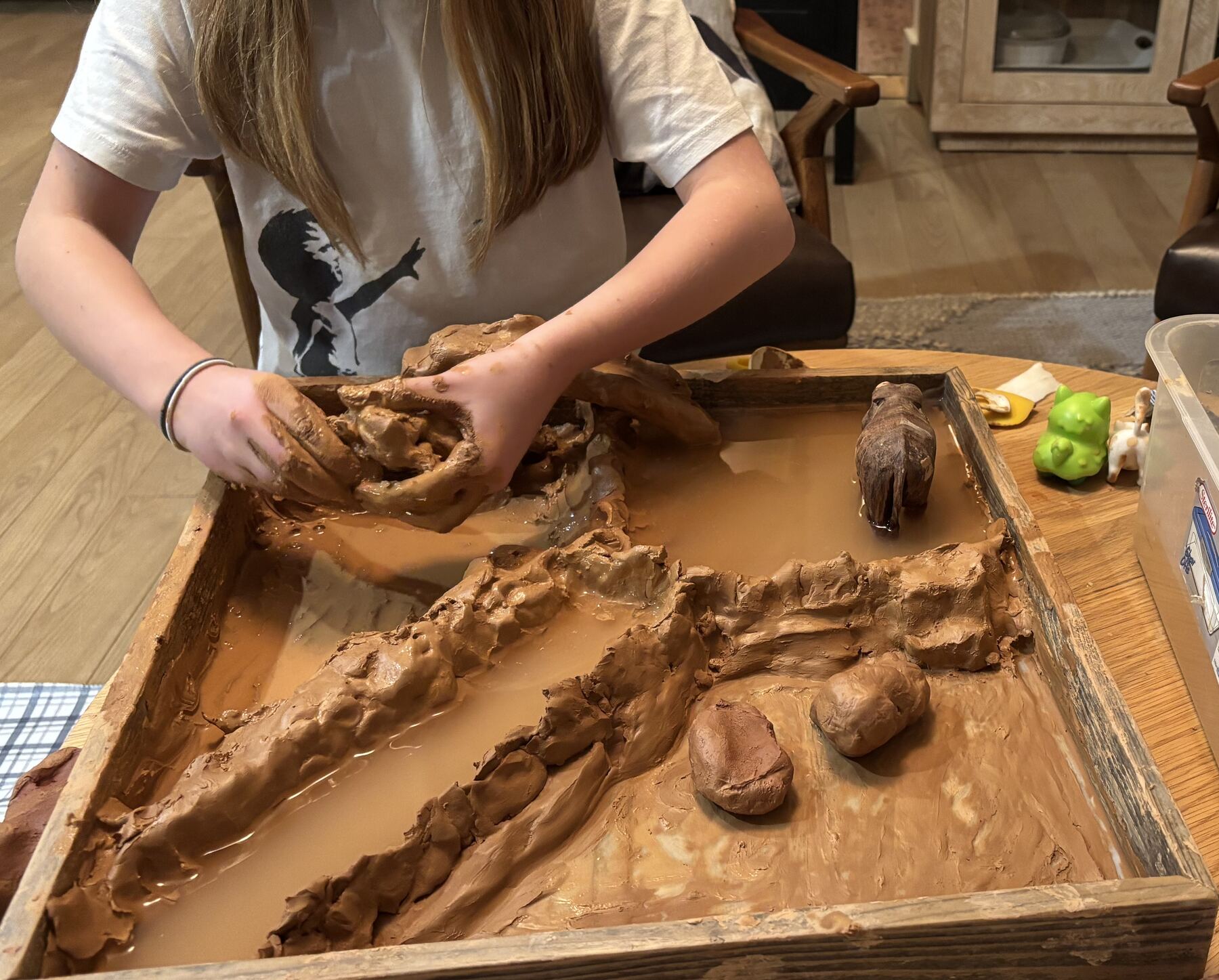 A child shaping wet clay in a tray during an art therapy activity.