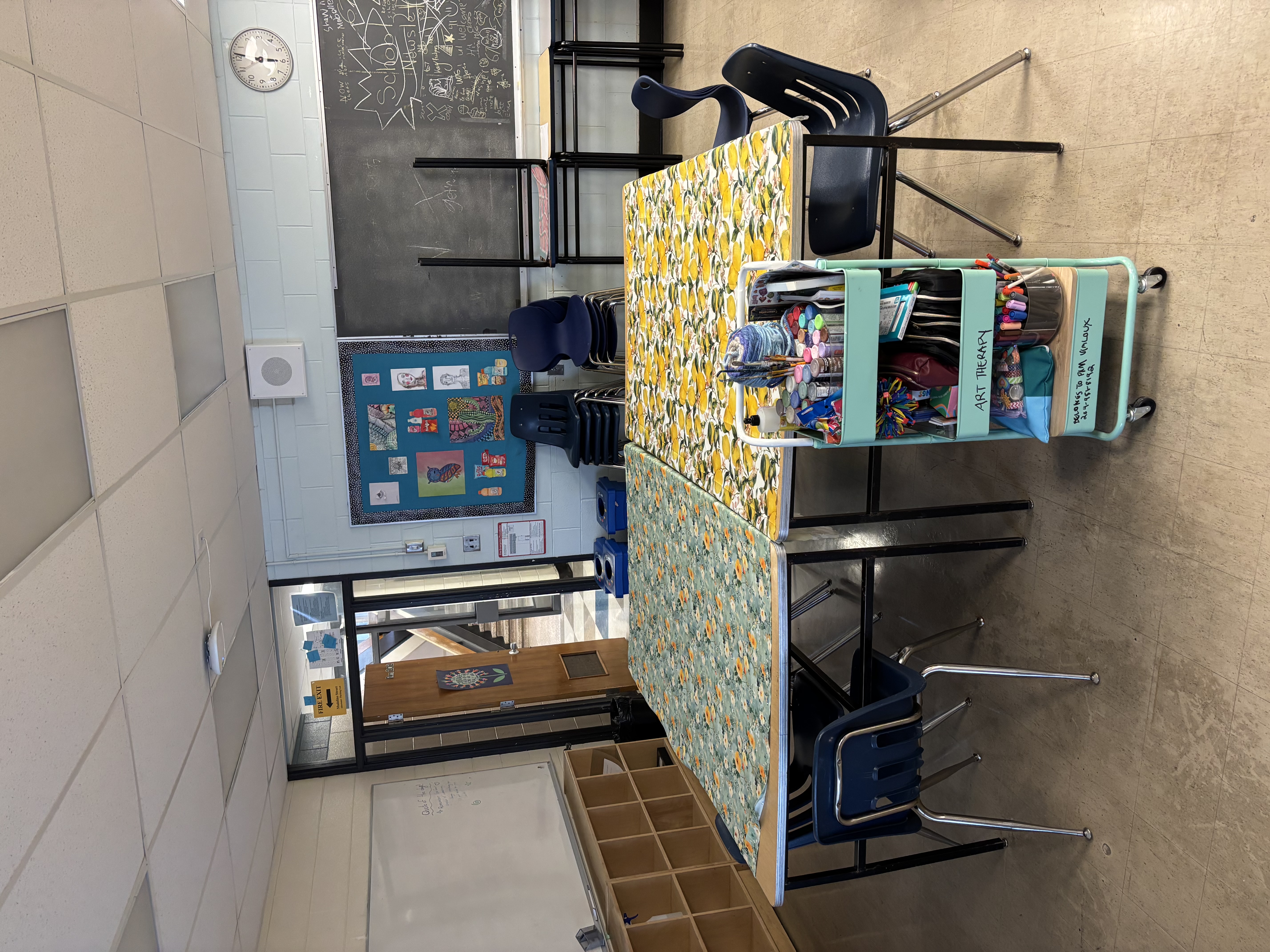 Art therapy classroom setup with supplies cart and children's artwork on the wall